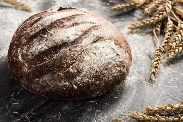 Pão fresco em um close-up da mesa em uma pitada de farinha e espigas de trigo, foco seletivo. comida saudável com massa fermentada e conceito tradicional de padaria. estilo sertanejo