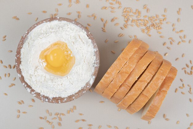 Pão fresco fatiado com uma tigela de madeira cheia de farinha. Foto de alta qualidade