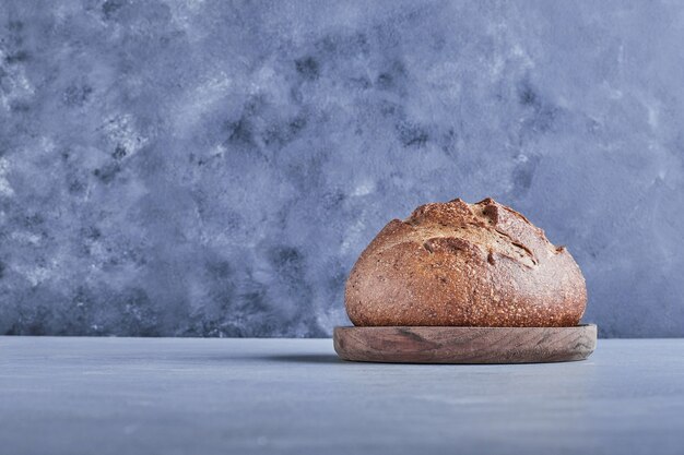 Pão redondo feito à mão na mesa cinza em uma bandeja de madeira.