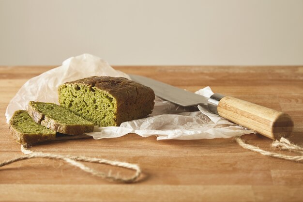 Pão saudável e rústico verde fatiado de massa de espinafre isolado com faca na tábua de madeira