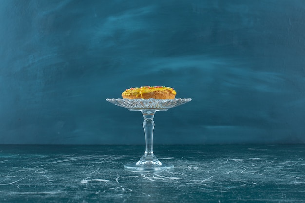 Foto grátis pãozinho doce coberto com gotas de chocolate em um pedestal de vidro, sobre o fundo azul. foto de alta qualidade