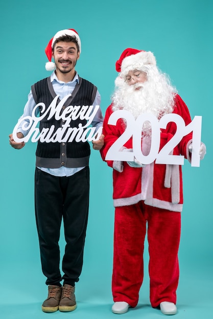 Papai Noel com um jovem segurando um feliz Natal e escritos sobre o fundo azul.