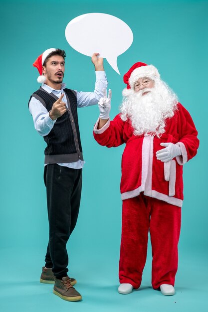 Papai Noel com um jovem segurando uma placa branca na mesa azul.