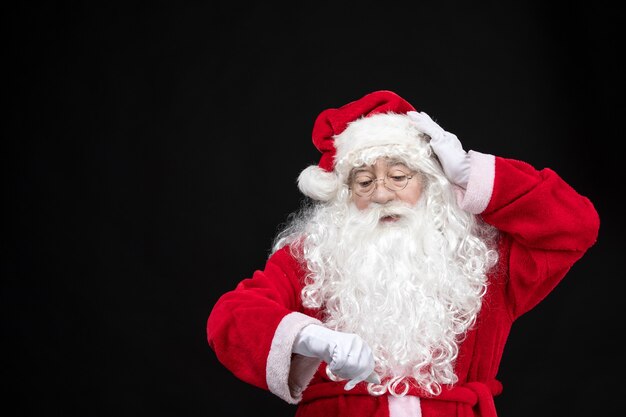Papai Noel em um terno clássico vermelho com barba branca na frente, verificando as horas
