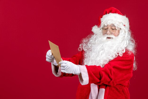 Papai Noel lendo uma carta de uma criança na mesa vermelha.