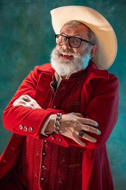 Papai noel moderno e elegante em um terno vermelho da moda e chapéu de cowboy no escuro