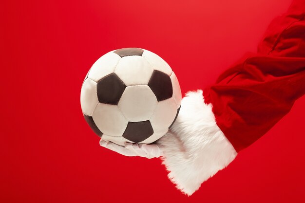 Papai Noel segurando uma bola de futebol isolada no fundo vermelho do estúdio