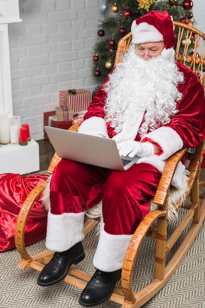 Foto grátis papai noel sentado na cadeira de balanço e trabalhando no laptop