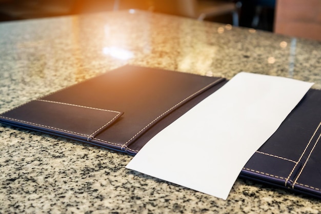 Papel branco vazio em branco na pasta de recibos de pagamento de restaurante na mesa de granito