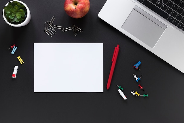 Papel de cartão branco em branco com caneta; maçã; artigos de papelaria de escritório colorido e laptop em fundo preto