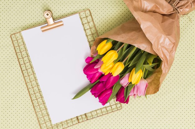 Papel em branco com clipboard e buquê de flores de tulipa sobre fundo amarelo de pontos