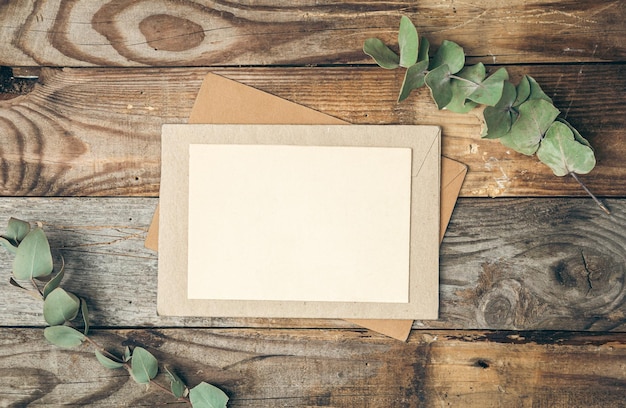 Papel em branco e envelope em fundo de madeira com galhos de eucalipto plano