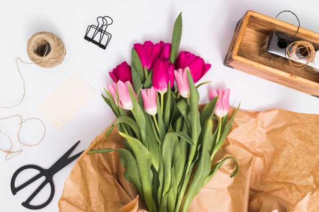 Papel pardo; flores de tulipa; corda; tesoura contra fundo branco
