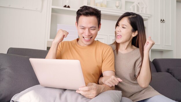 Par asiático, usando computador portátil, para, busca, teia, em, sala de estar, casa