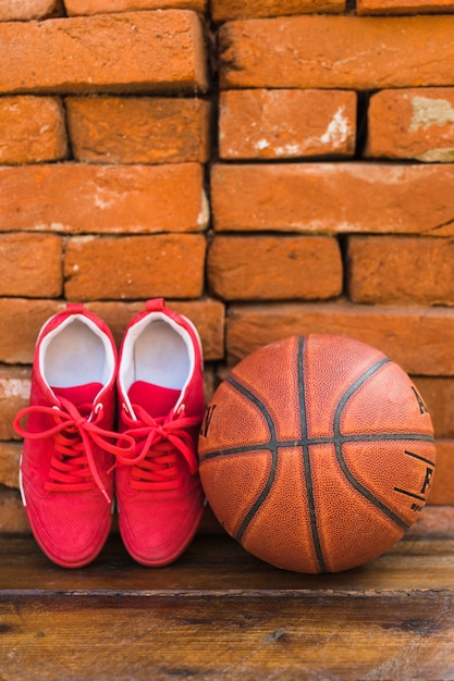 Par de sapatas do esporte e basquete na mesa de madeira contra a pilha de parede de tijolo