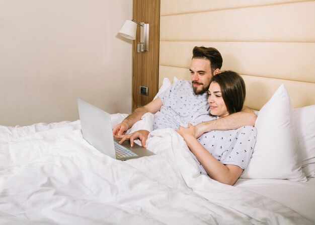 Par jovem, cama, usando computador portátil