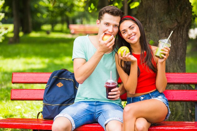 Par jovem, sentando, ligado, banco, segurando, alimento saudável, e, smoothies, parque