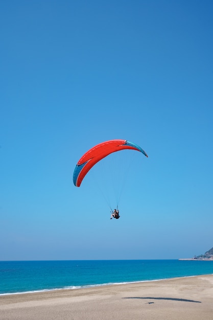 Paraglider tandem voando sobre a costa do mar com água azul e o céu em horison. Vista do parapente e da lagoa azul na Turquia.