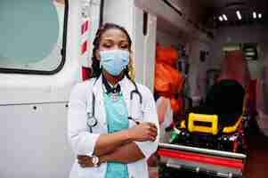 Foto grátis paramédica afro-americana em máscara médica protetora facial em frente ao carro da ambulância