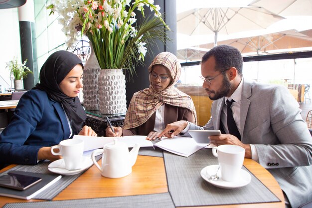 Parceiros de negócios multiculturais discutindo contrato no café