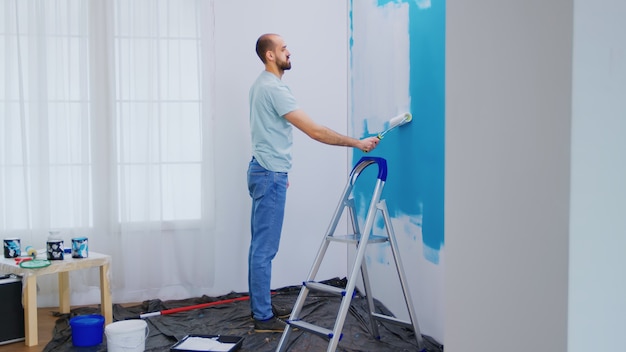 Parede de pintura de faz-tudo com escova de rolo mergulhada em tinta branca. Faz-tudo renovando. Redecoração de apartamento e construção de casa durante a reforma e melhoria. Reparação e decoração.