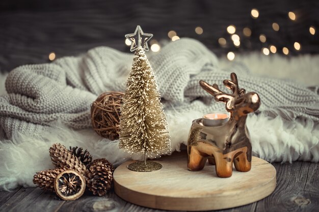 Parede festiva de Natal com cervo de brinquedo com caixa de presente e árvore de Natal, parede desfocada com luzes douradas na mesa de deck de madeira