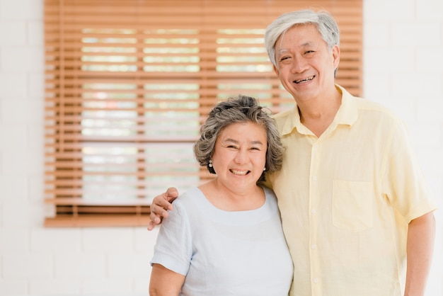 Pares idosos asiáticos que sentem o sorriso feliz e que olham à câmera quando relaxam na sala de visitas em casa.