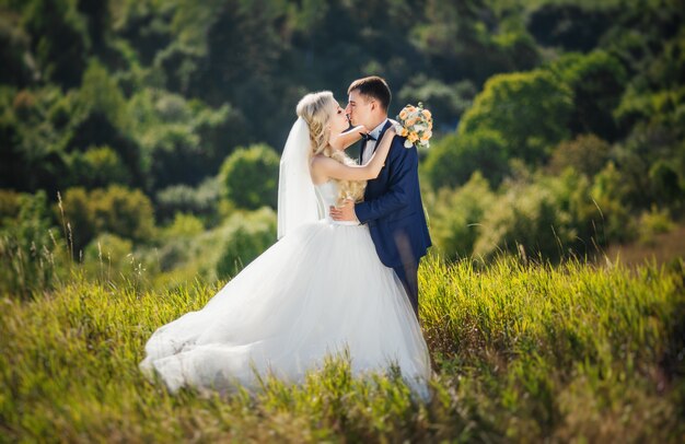 Pares novos no amor, no noivo e na noiva no vestido de casamento que beijam na natureza.