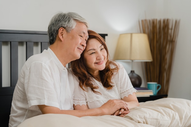 Pares sênior asiáticos que falam na cama em casa. As avós, o marido e a esposa chineses sênior asiáticos felizes relaxam junto após acordam ao encontrar-se na cama no quarto em casa no conceito da manhã.