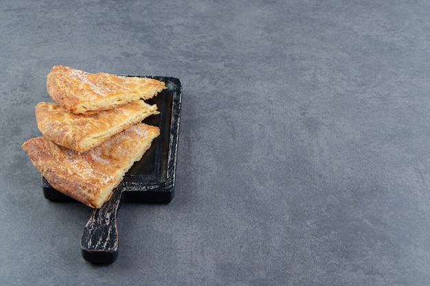 Pastelaria em forma de triângulo na placa de corte preta.