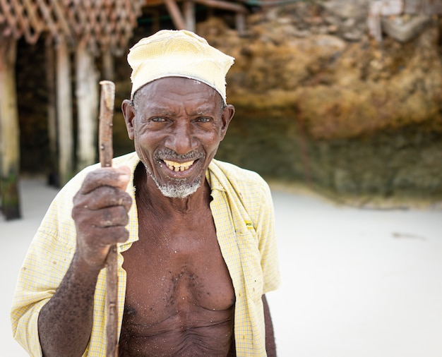 Pastor africano idoso caminhando na praia segurando uma bengala