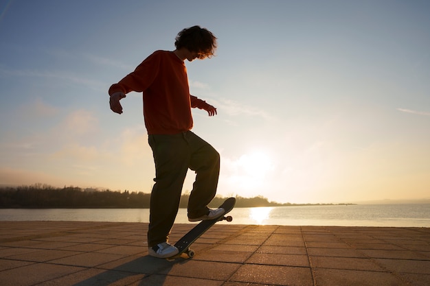 Patinador de tiro completo posando ao pôr do sol