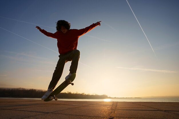 Patinador de tiro completo posando ao pôr do sol