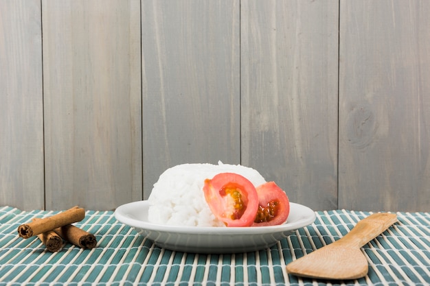 Paus de canela; espátula e prato de arroz branco com fatia de tomate no placemat