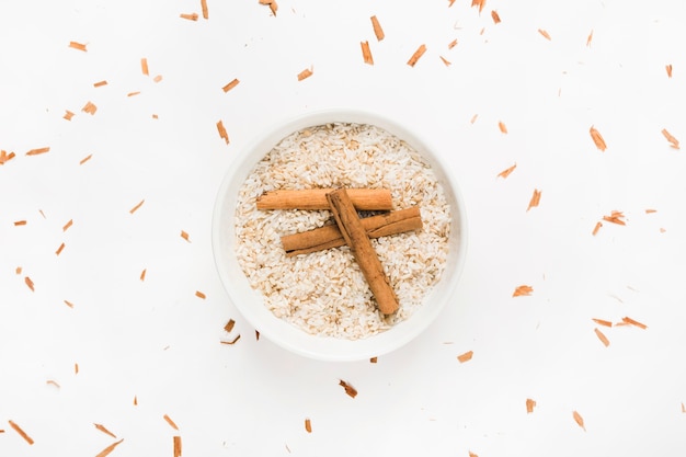 Paus de canela na tigela de arroz cru sobre fundo branco