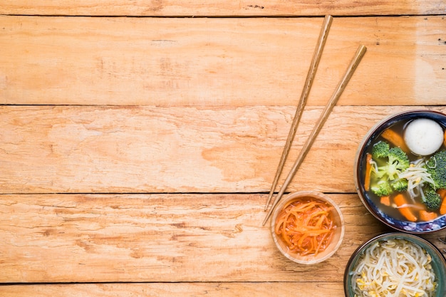 Pauzinhos com cenoura ralada; brotar feijão e sopa de bola de peixe na mesa de madeira
