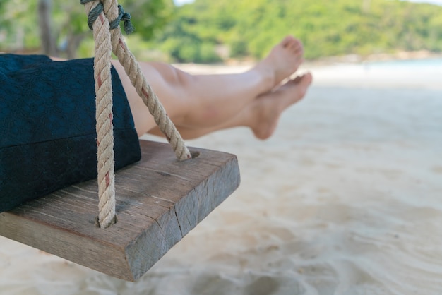 Pé da mulher em um balanço na praia do mar tropical