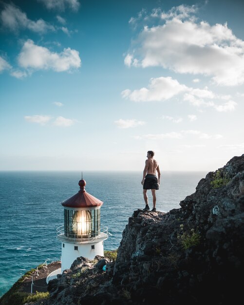 Pé masculino sem camisa em um penhasco rochoso perto de um farol e o mar