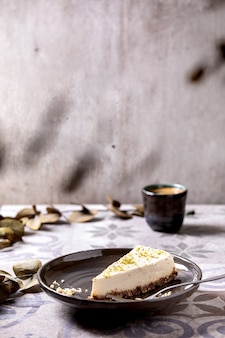 Pedaço de cheesecake vegan cru, sem asse sem glúten, decorado com raspas de limão e castanhas de caju no prato