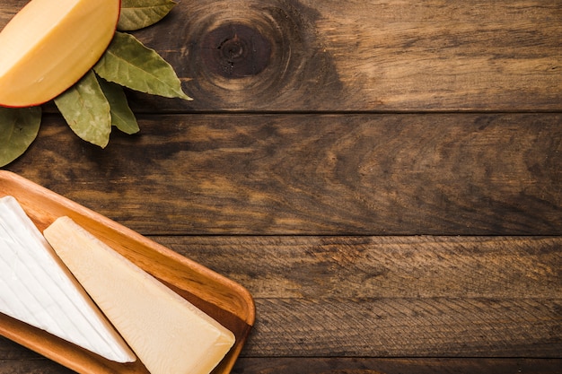 Pedaço de queijo na bandeja de madeira com folhas de louro contra a mesa de madeira