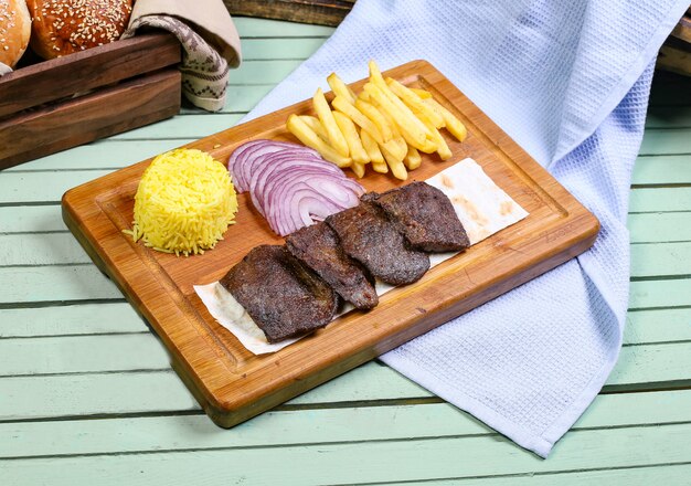 Pedaços de bife de carne com batatas fritas, cebola e arroz.