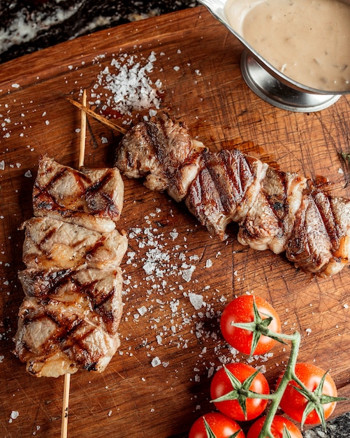 Foto grátis pedaços de bife grelhado no espeto de bambu, guarnecido com sal e tomate