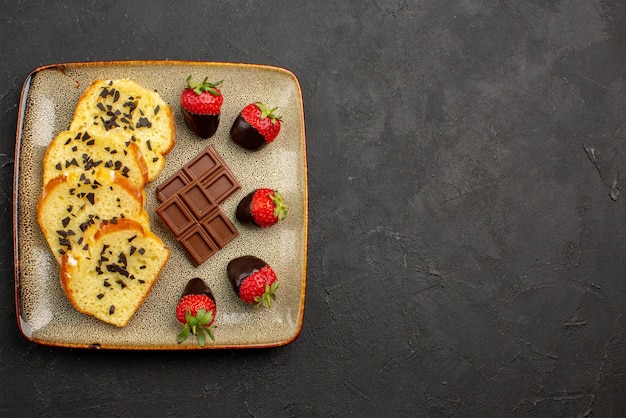 Pedaços de bolo apetitosos pedaços de bolo apetitosos com chocolate e morangos no lado esquerdo da mesa escura