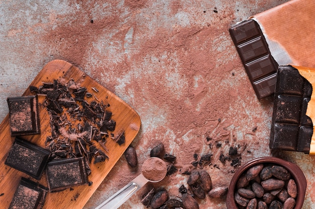 Pedaços de chocolate, bar e cacau em pó e feijão tigelas na mesa bagunçada