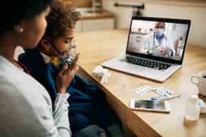 Foto grátis pediatra negra falando por videochamada com a mãe que está dando terapia de inalação à filha em casa