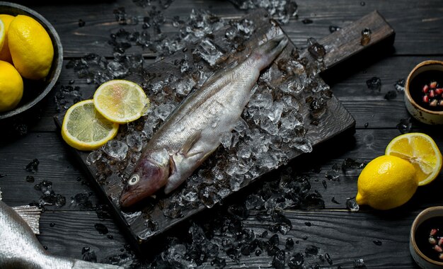 Peixe fresco em uma placa de madeira com cubos de gelo e limão