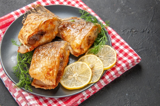 Foto grátis peixe frito com rodelas de limão no prato e guardanapo em fundo preto.