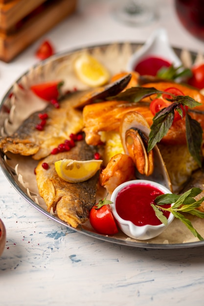 Foto grátis peixe grelhado assado e frutos do mar servidos com ervas, limão e molho de tomate vermelho.