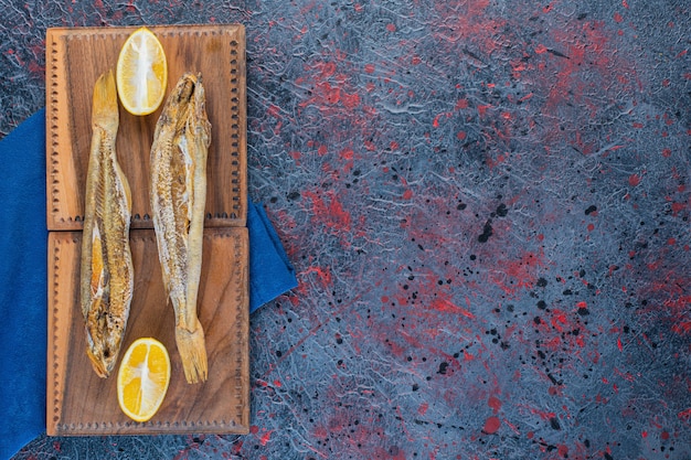 Foto grátis peixe seco salgado com uma rodela de limão isolado em uma placa de madeira