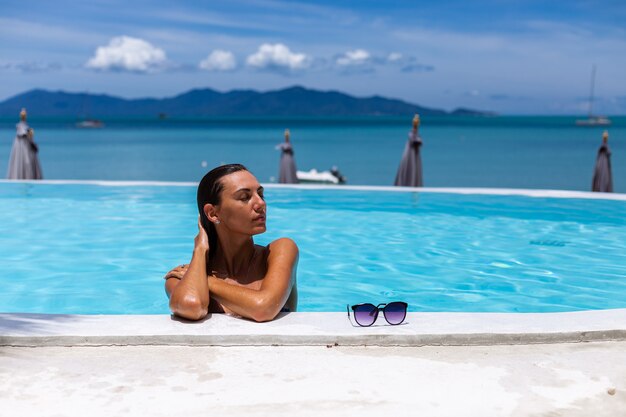 Pele bronzeada brilhante de mulher caucasiana bronzeada à beira da piscina em biquíni azul em dia de sol